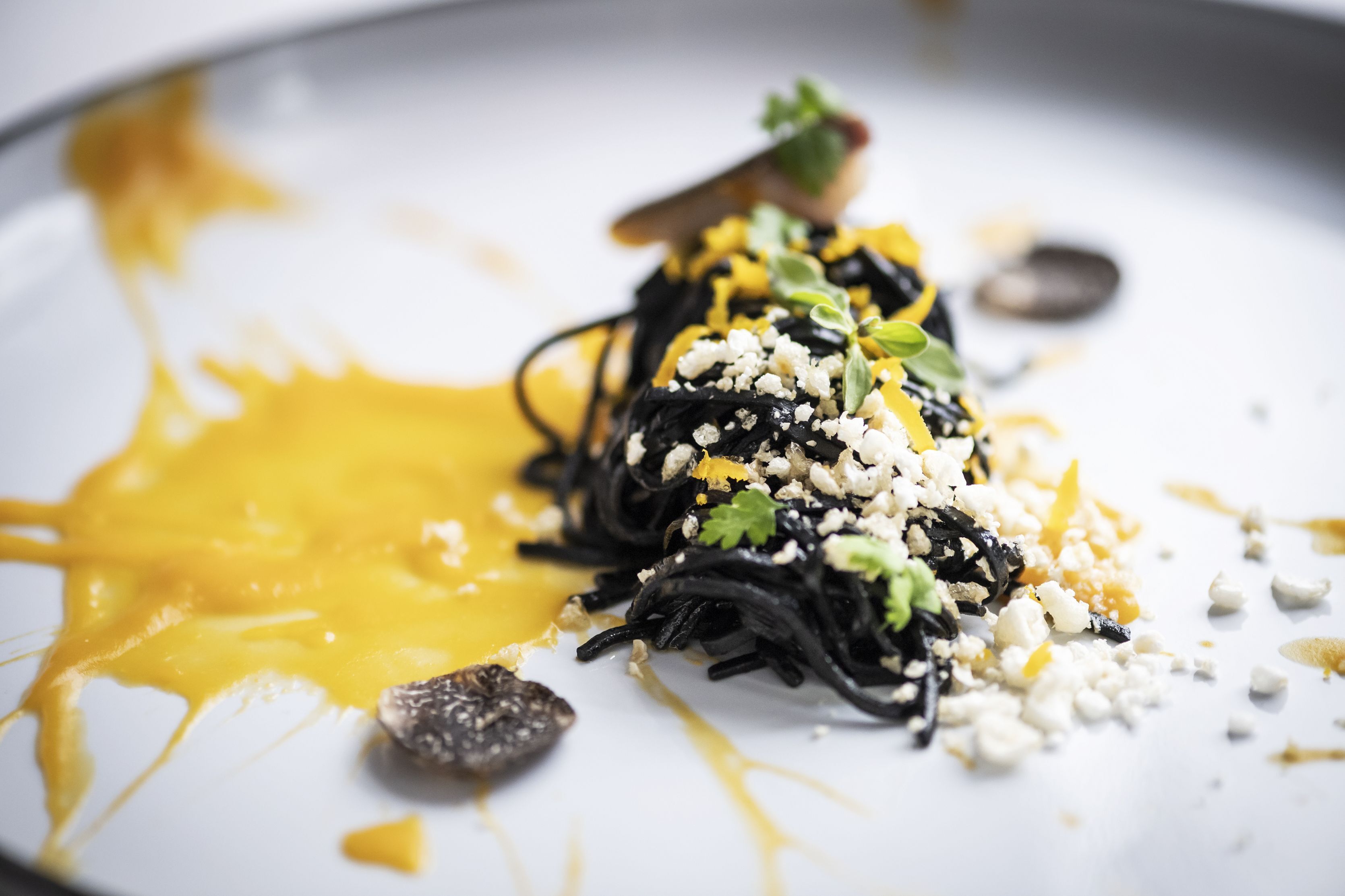 A plate of black pasta with yellow sauce, cheese, and herbs.