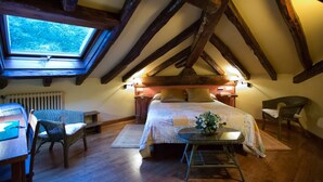 A cozy attic bedroom with a skylight, wooden beams, a bed, two wicker chairs, a small table with a vase, and a radiator. - Hotel Rural Irigoienea (Urdax)