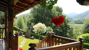 A wooden balcony with a view of a lush garden and distant mountains. - Hotel Rural Irigoienea (Urdax)
