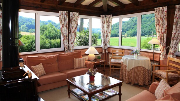 A cozy living room with a sofa, coffee table, and a fireplace. Large windows offer a view of the outdoors. - Hotel Rural Irigoienea (Urdax)
