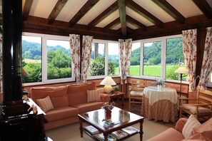 Un salon chaleureux avec un canapé, une table basse et une cheminée. De grandes fenêtres offrent une vue sur l’extérieur.