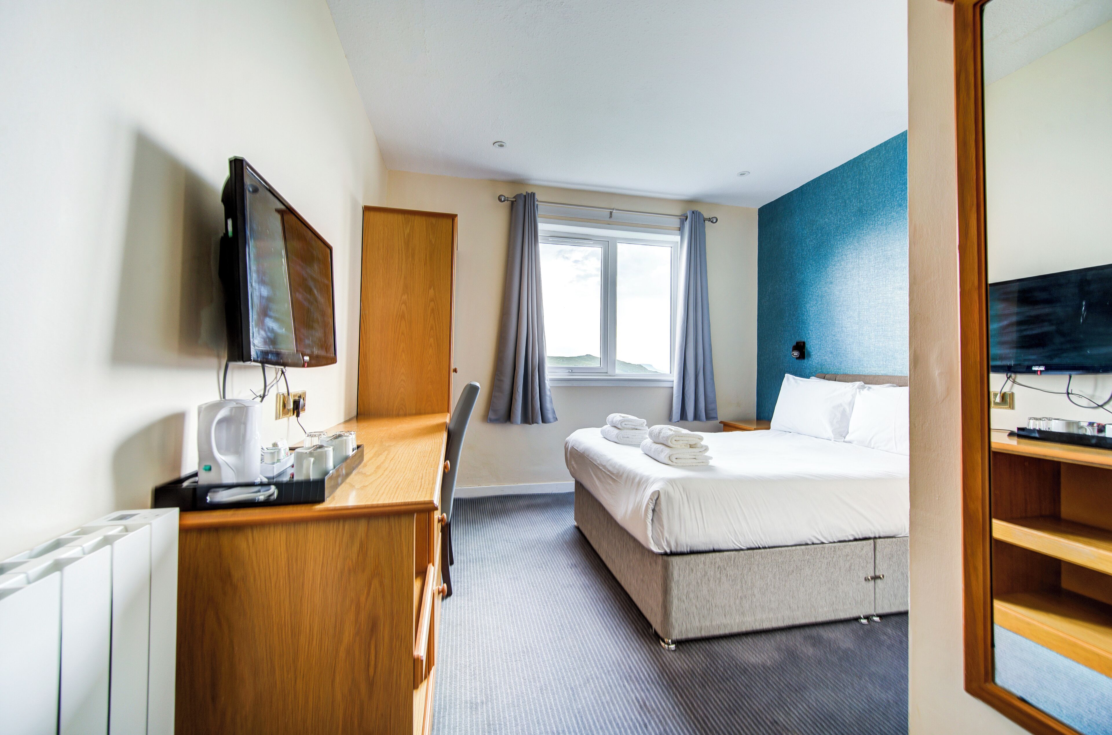A hotel room with a bed, a desk with a computer, a television, and a window with curtains.