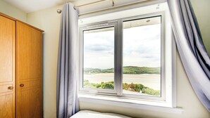 A bedroom with a large window offering a view of a beach and hills. - Morar Hotel (Mallaig)