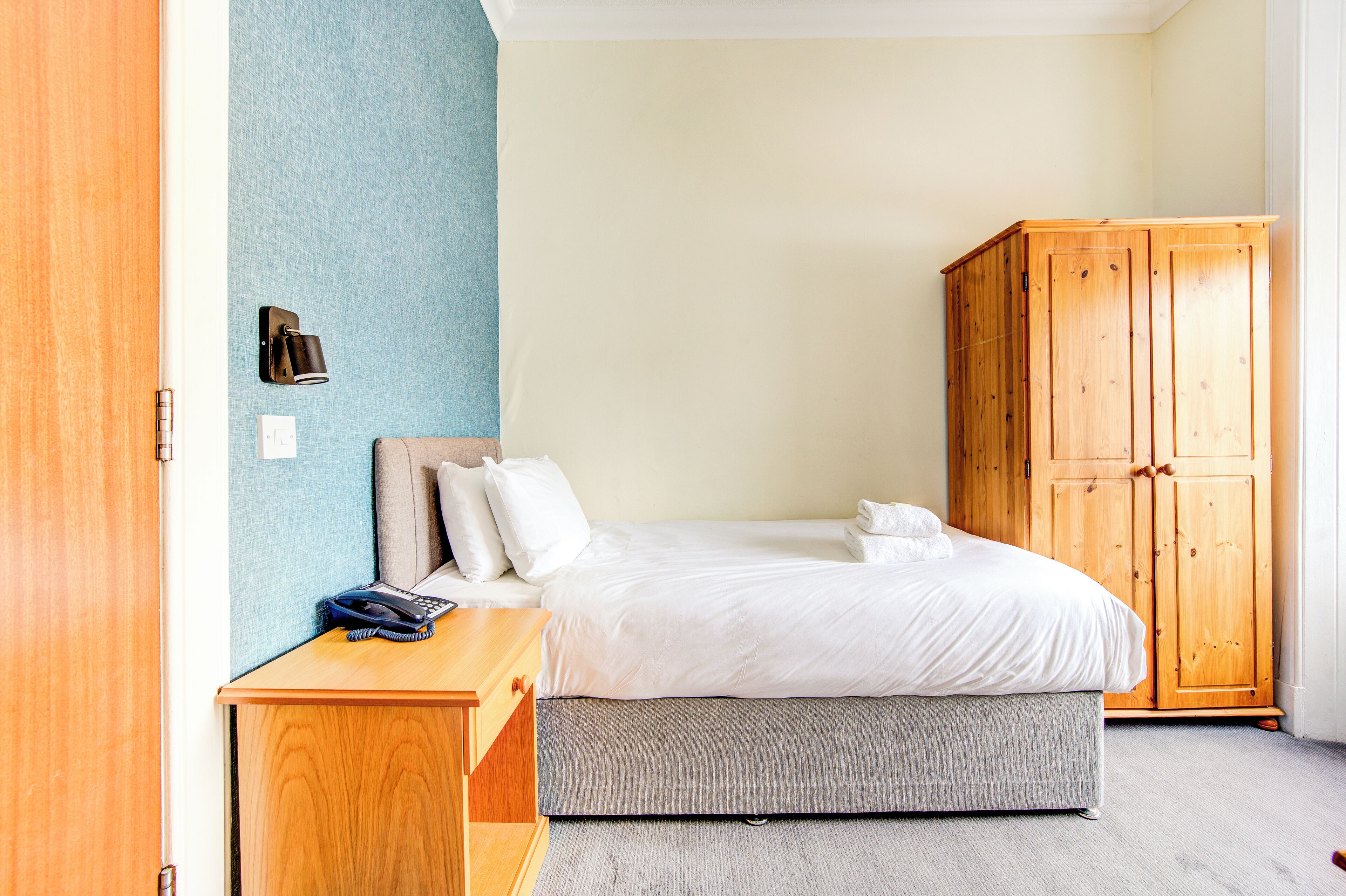 Un dormitorio con cama, un armario de madera, una mesita de noche con lámpara y una pared azul.