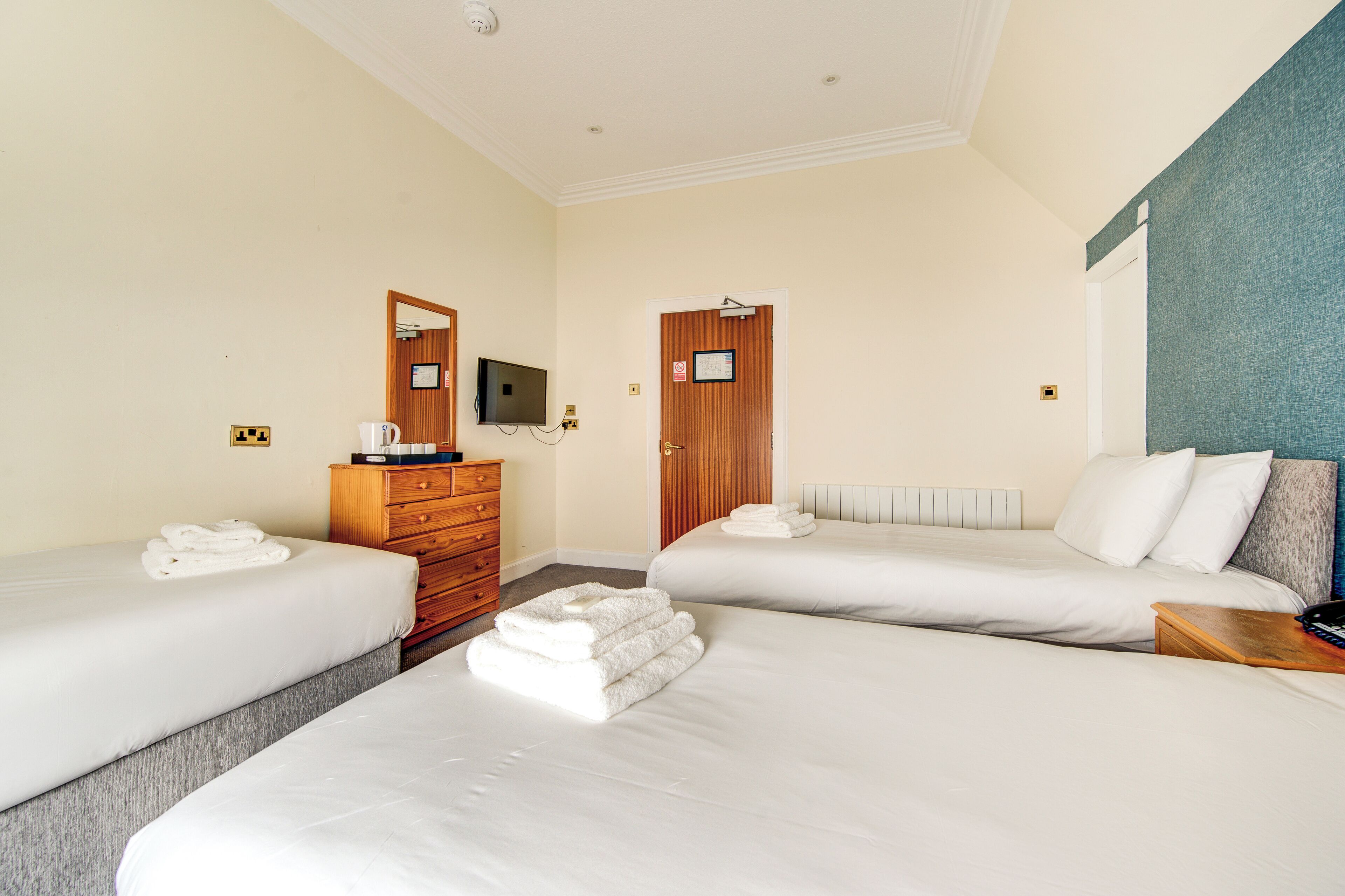 A hotel room with two single beds, a wooden dresser, a television, and a door with a sign.