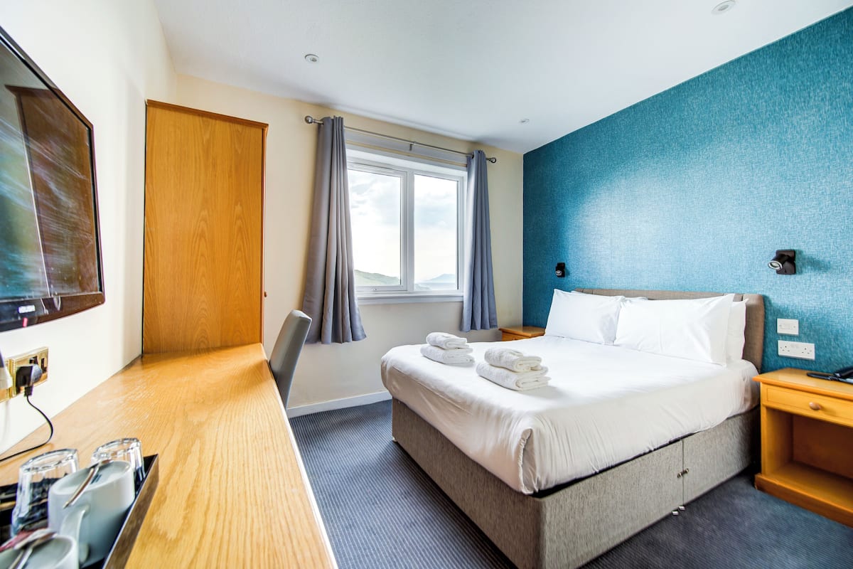 Quarto de hotel com cama, mesa de cabeceira e escrivaninha com cadeira.