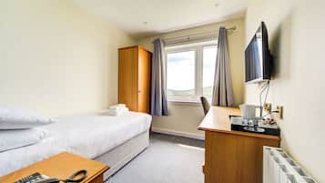 Ein Hotelzimmer mit einem Bett, einem Schreibtisch mit Telefon, einem Fernseher und einem Fenster mit Vorhängen.