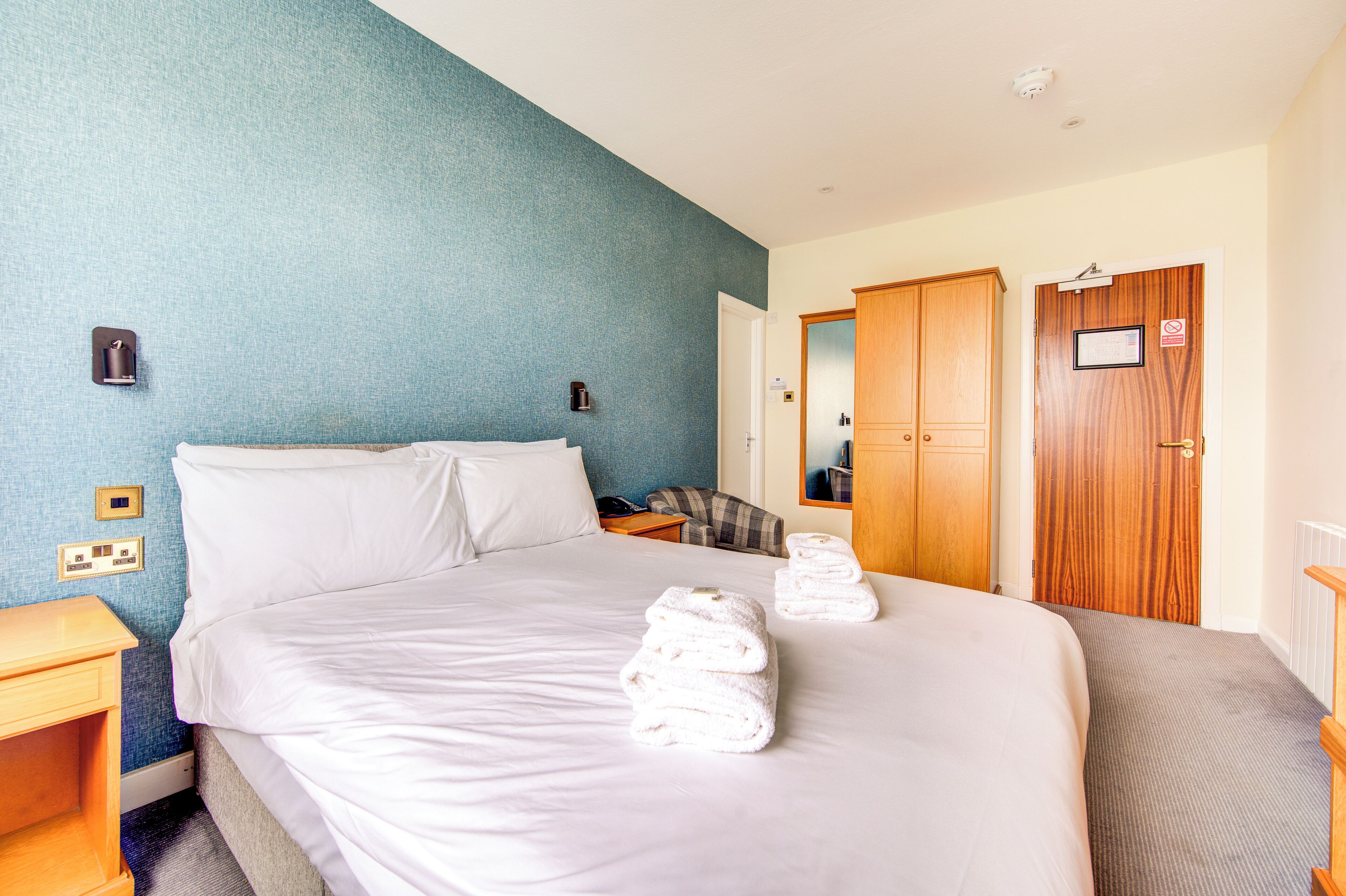 Une chambre d’hôtel avec un grand lit, une table de chevet, une chaise et une armoire en bois.