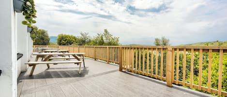 A wooden deck with picnic tables and a wooden railing overlooking a green landscape.
