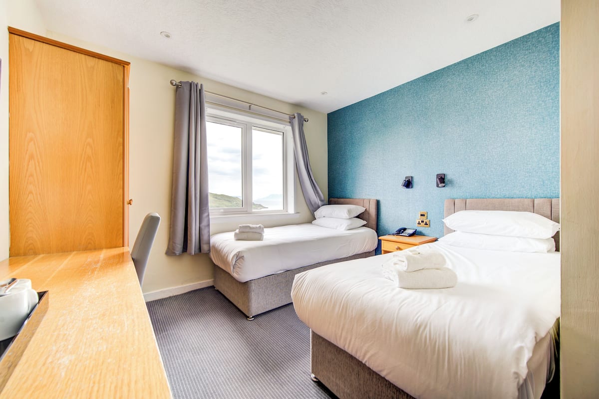 Quarto de hotel com duas camas, uma escrivaninha e uma janela com cortinas.