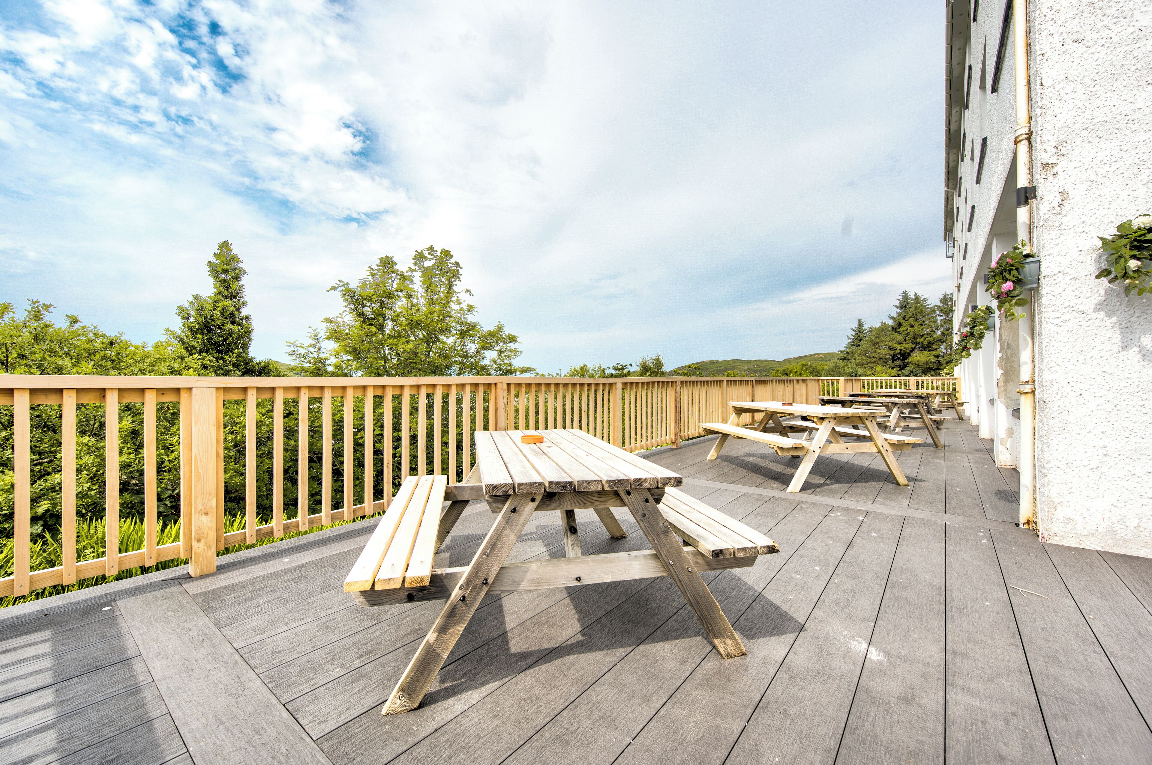 Una terraza al aire libre con mesas de picnic, una valla de madera y un edificio de fachada blanca.