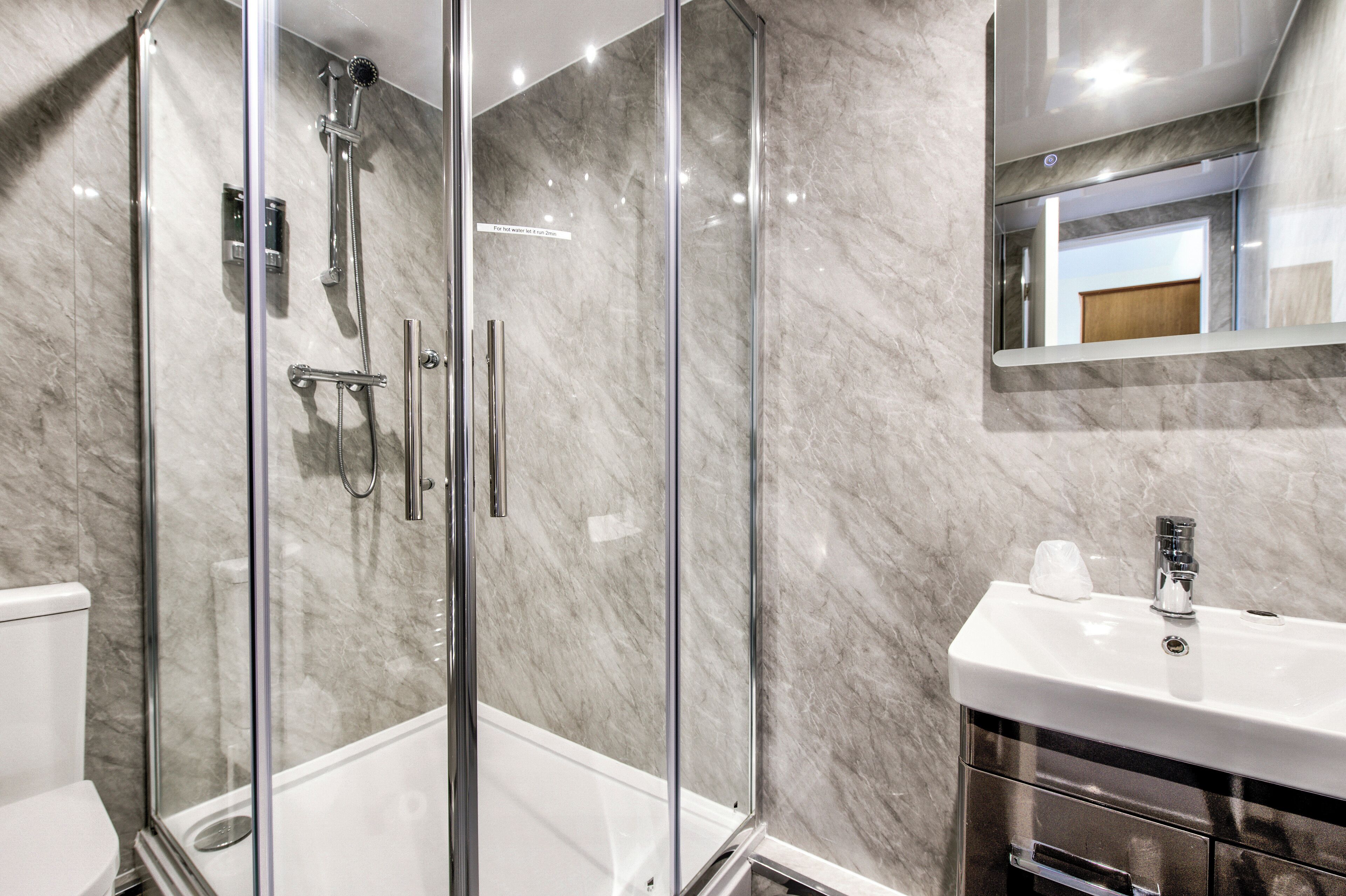 A modern bathroom with a glass-enclosed shower, a white sink, and a marble backsplash.