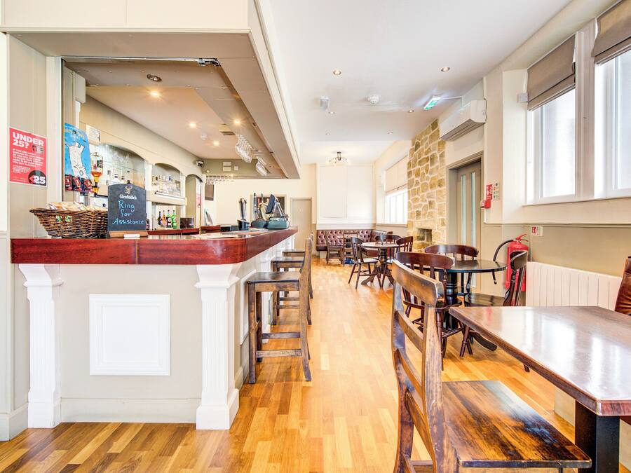 Un restaurant doté d’un bar, de planchers en bois et offrant différents types de sièges, notamment des banquettes et des tables.