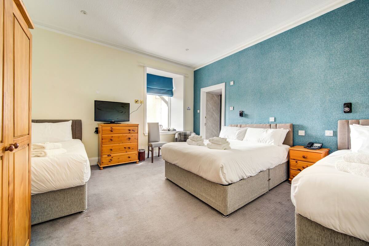 Quarto de hotel com duas camas, televisão, cómoda de madeira e uma cadeira.