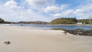 A sandy beach with a calm body of water, a boat, and a signpost in the distance. - Morar Hotel (Mallaig)