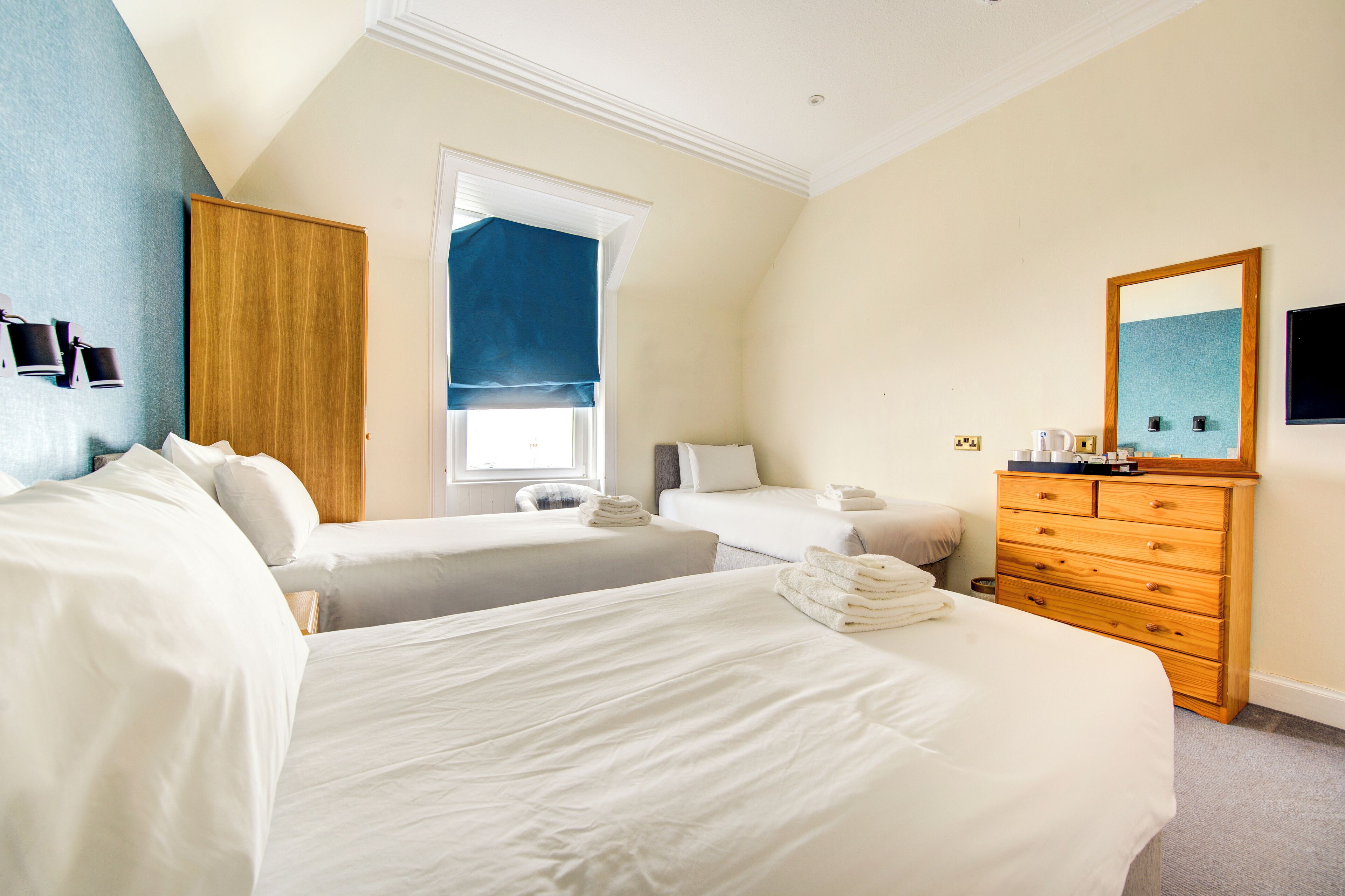 Habitación de hotel con dos camas, un aparador de madera, un espejo grande y una ventana con cortina azul.