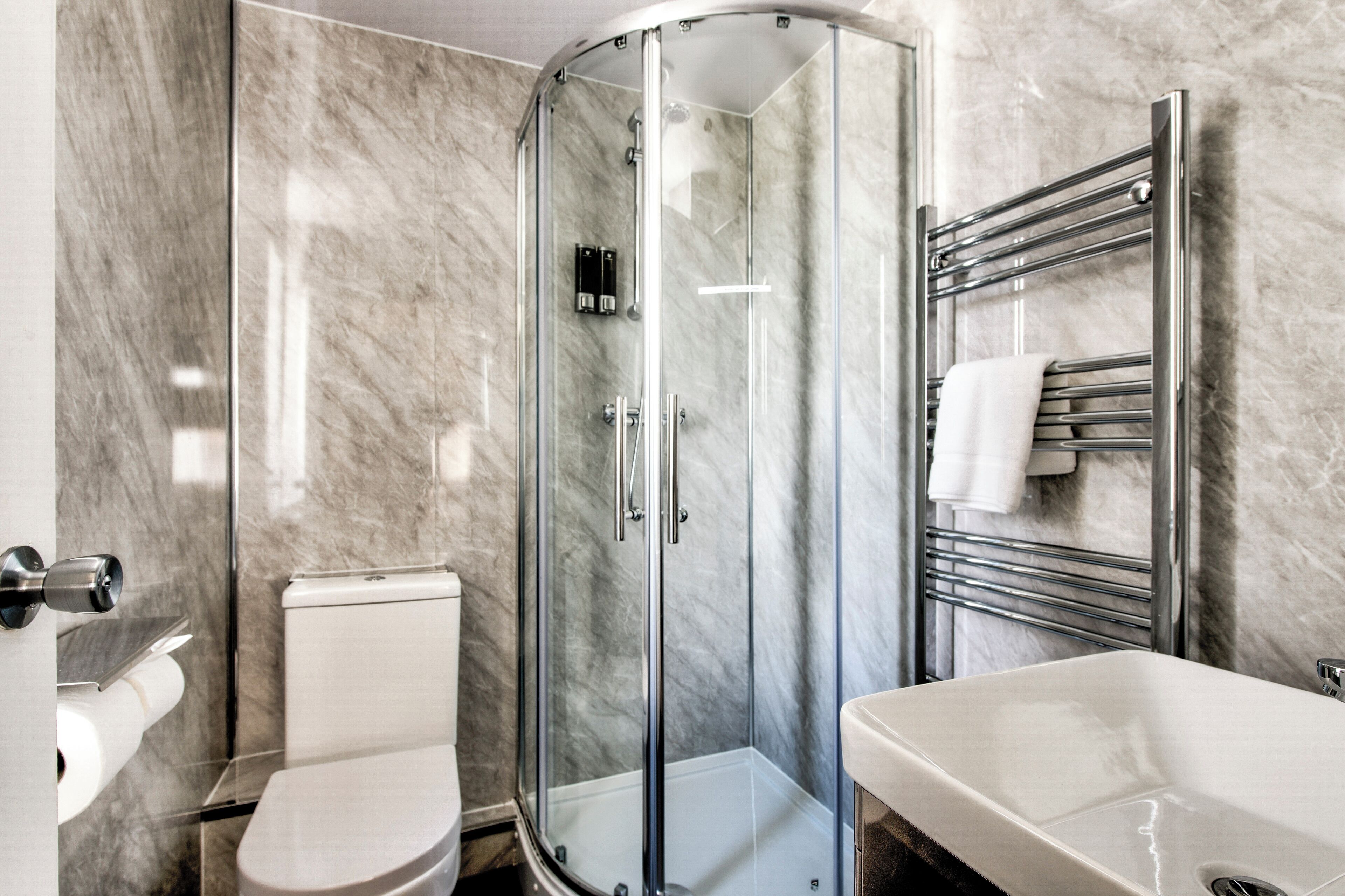 A modern bathroom with a glass-enclosed shower, a white toilet, and a sink with a chrome towel rack.