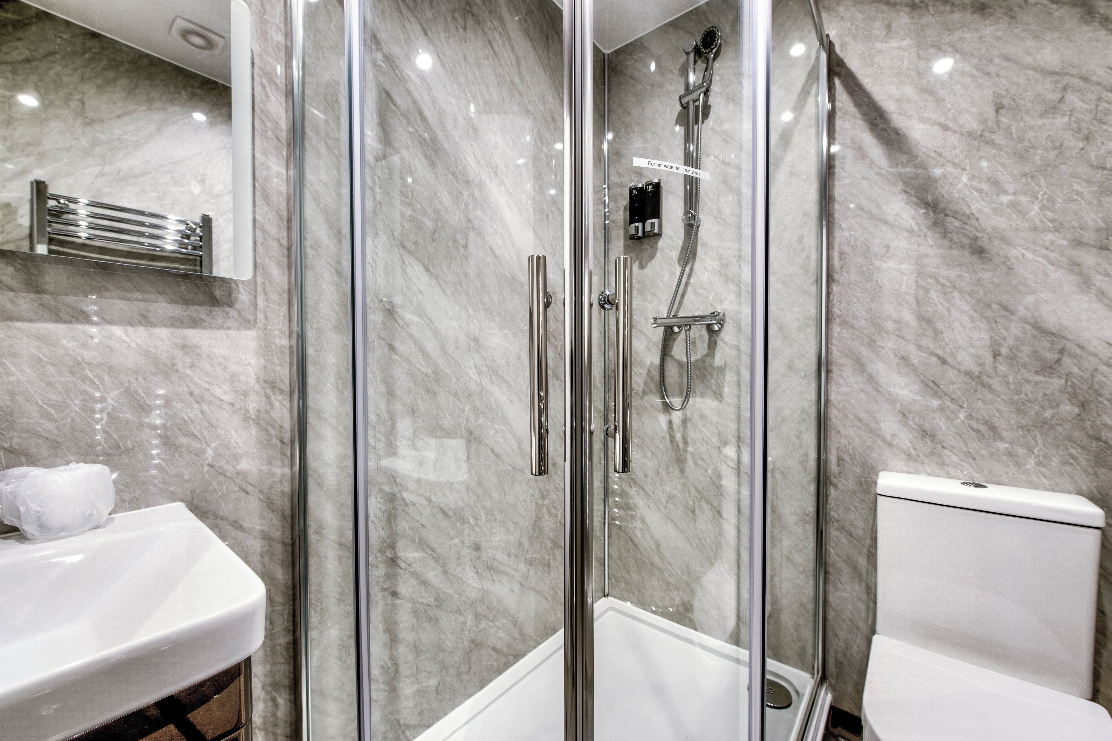 A modern bathroom with a glass-enclosed shower, a white sink, and a toilet.