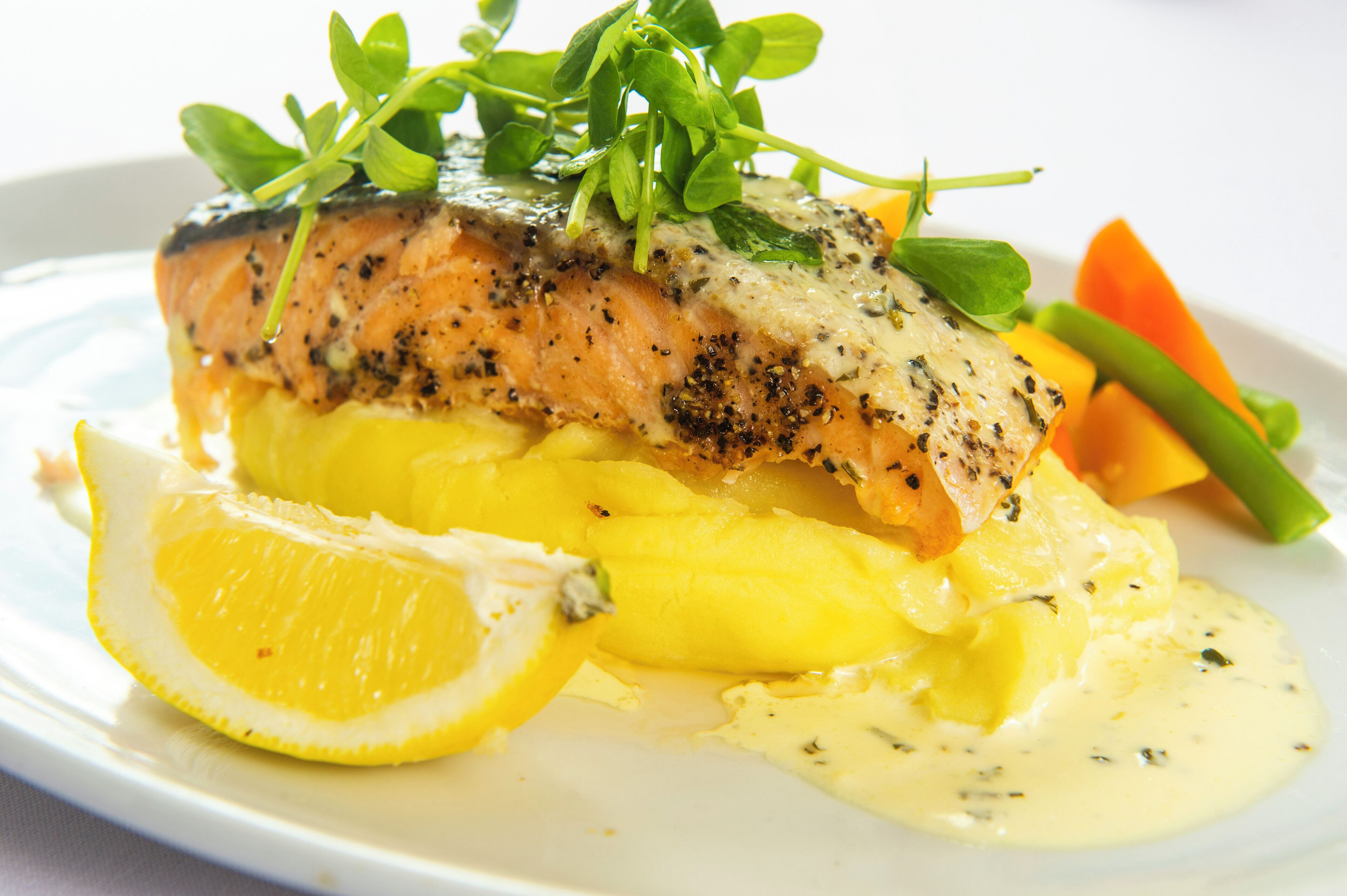 Een bord met zalm, gepureerde aardappelen, een citroenpartje en groenten.