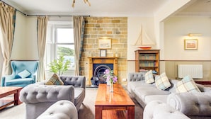 A cozy living room with a fireplace, comfortable seating, a bookshelf, and a view of the outdoors. - Morar Hotel (Mallaig)