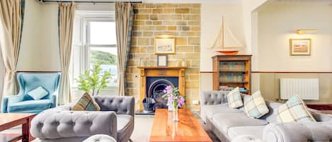 Una sala de estar acogedora con chimenea, asientos cómodos, una estantería y vistas al exterior.