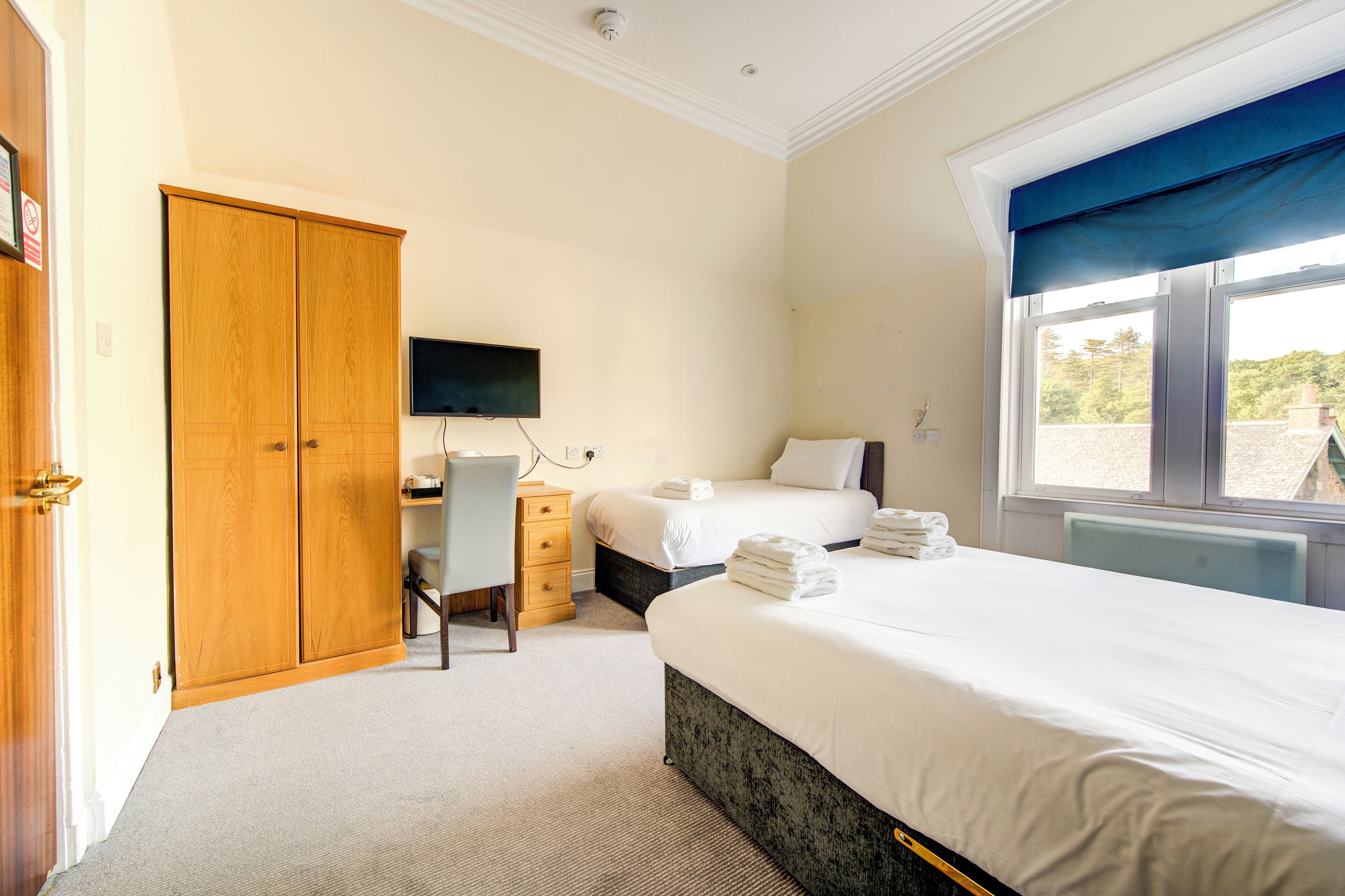 Habitación de hotel con cama, escritorio, silla, armario y televisor.