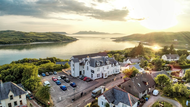 A hotel with a parking lot, surrounded by greenery and a body of water. - Morar Hotel (Mallaig)