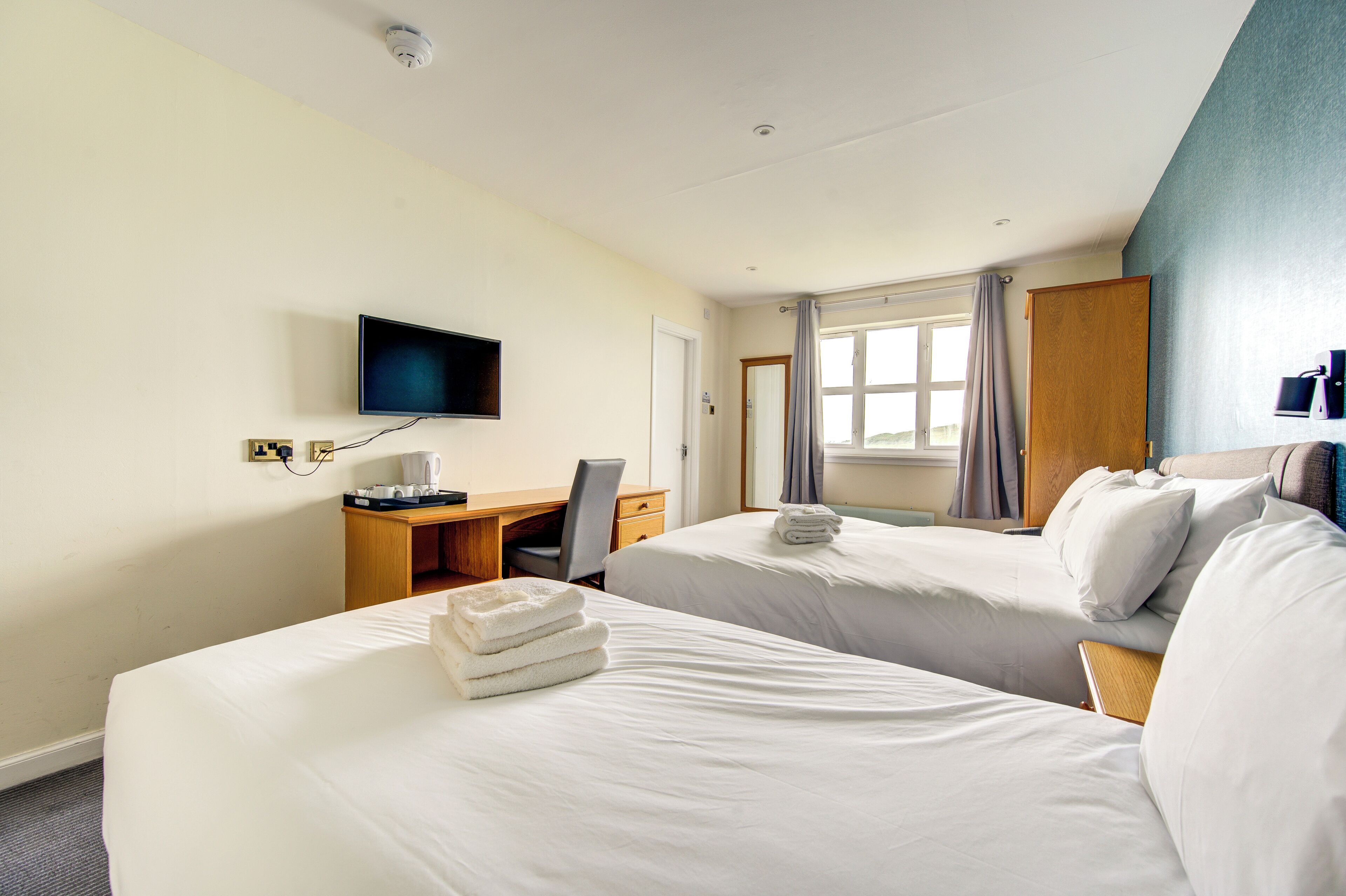 Ein Hotelzimmer mit zwei Betten, einem Schreibtisch, einem Sessel, einem Fernseher und einem Fenster mit Vorhängen.