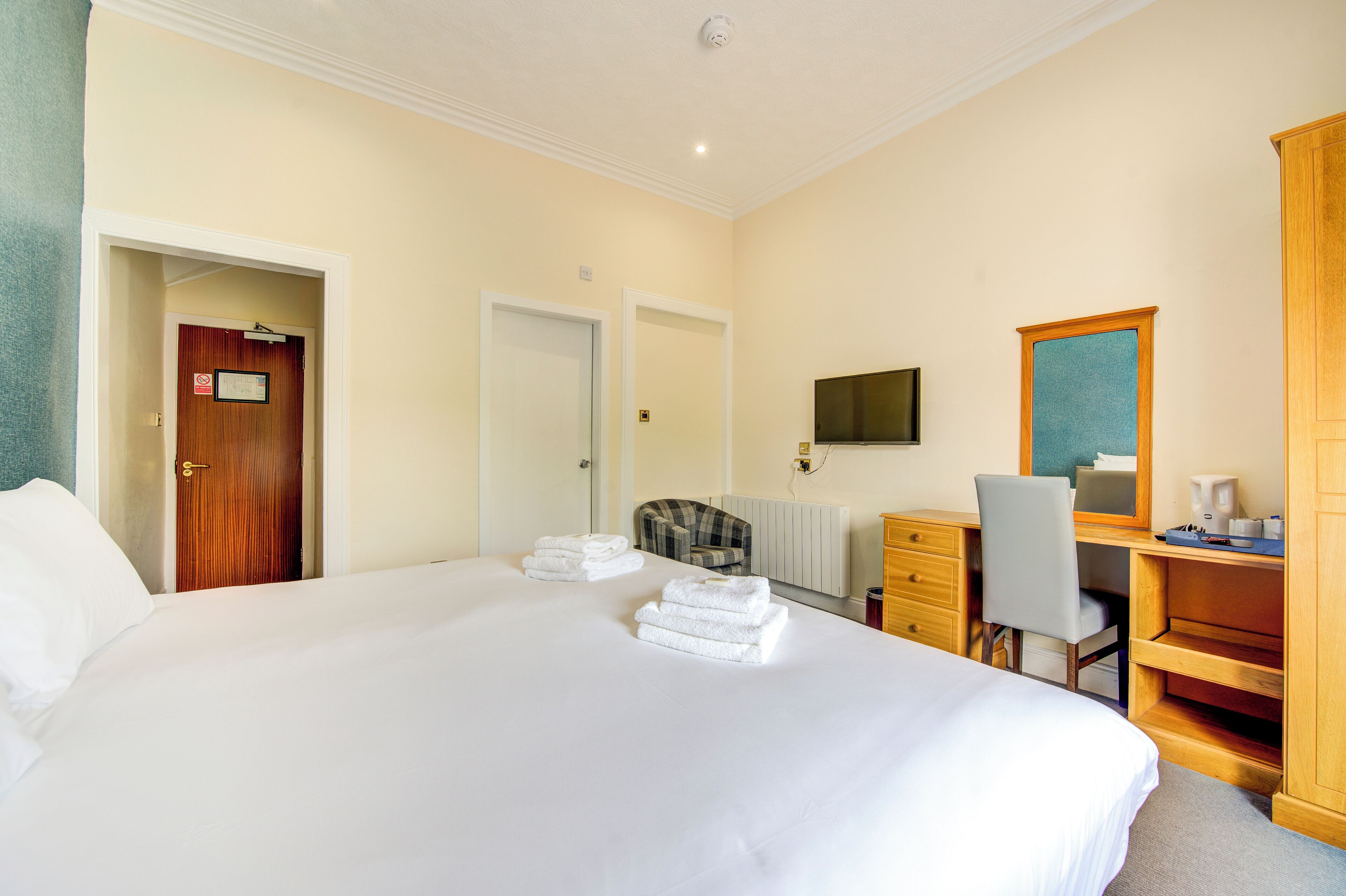 Een hotelkamer met een groot bed, een bureau met stoel, een televisie en een kledingkast.
