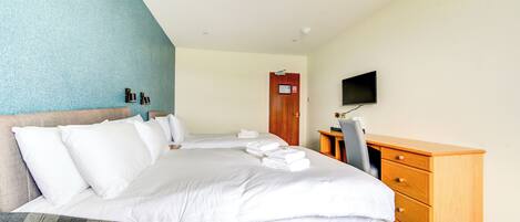 A hotel room with a large bed, a wooden dresser, a television, and a door with a sign.
