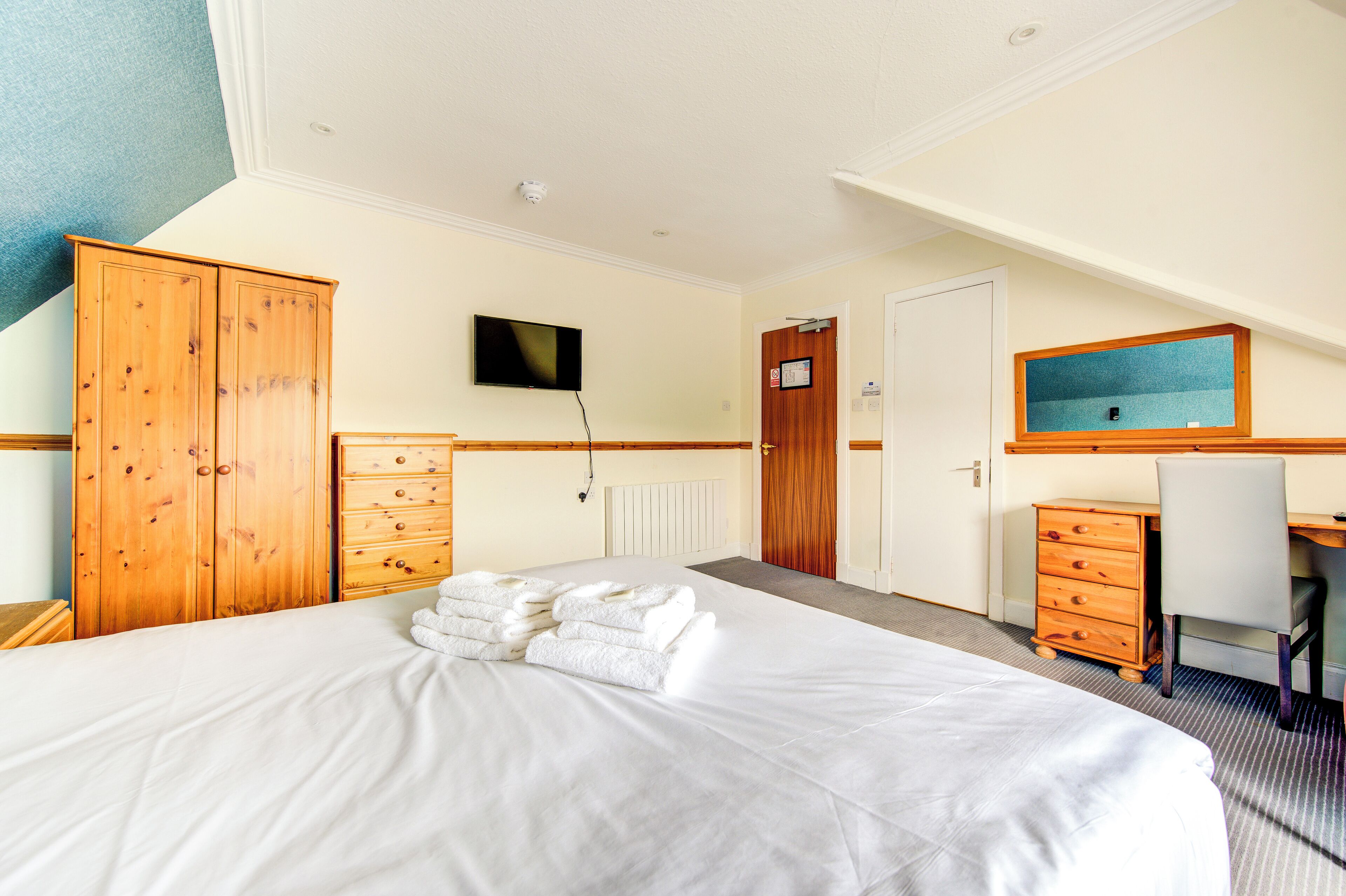Ein Hotelzimmer mit einem großen Bett, einem Holzschrank, einem Schreibtisch mit Stuhl, einem Fernseher und einem gerahmten Bild an der Wand.