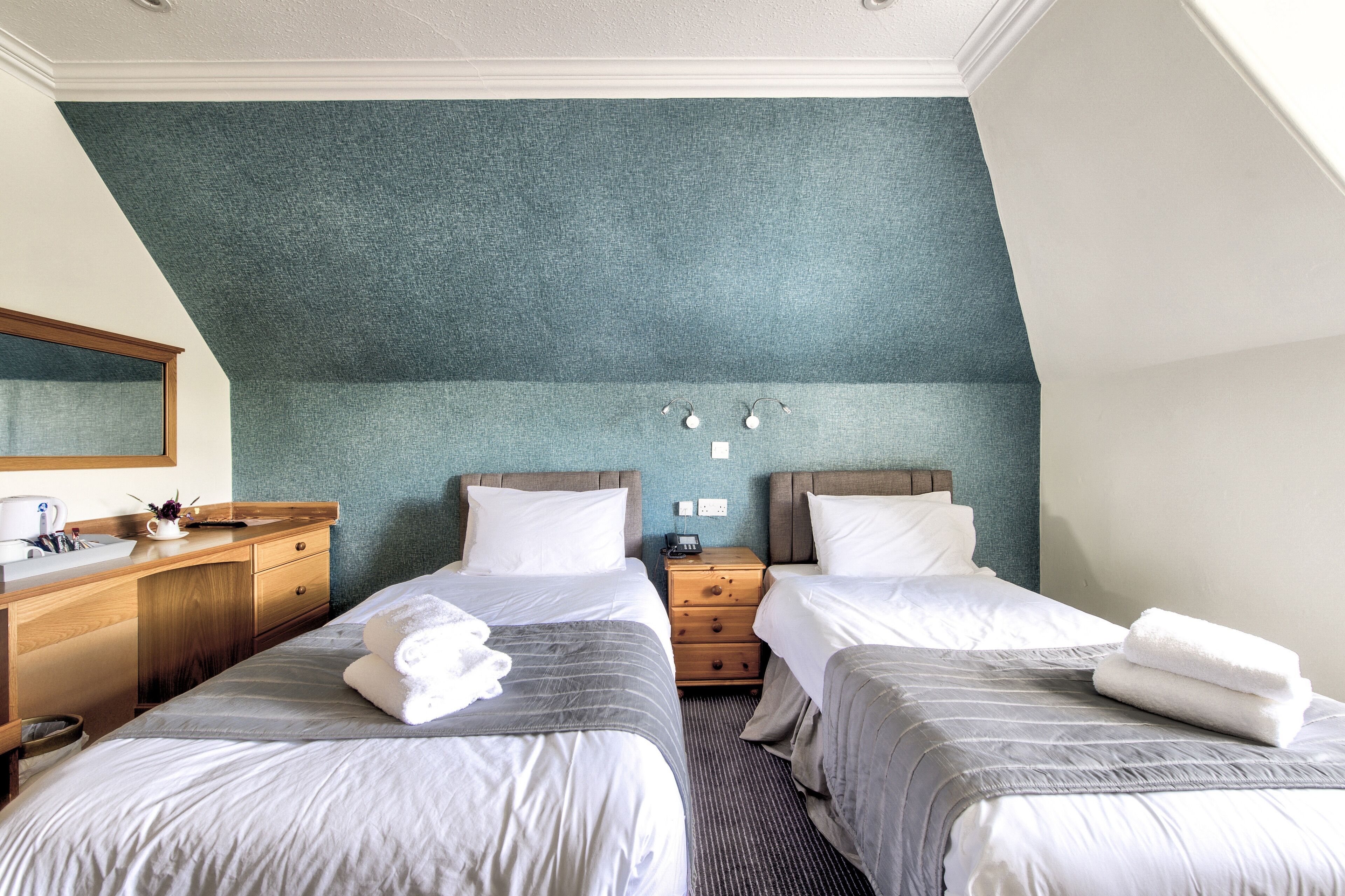 A hotel room with two beds, a wooden dresser, a mirror, and a blue textured wall.