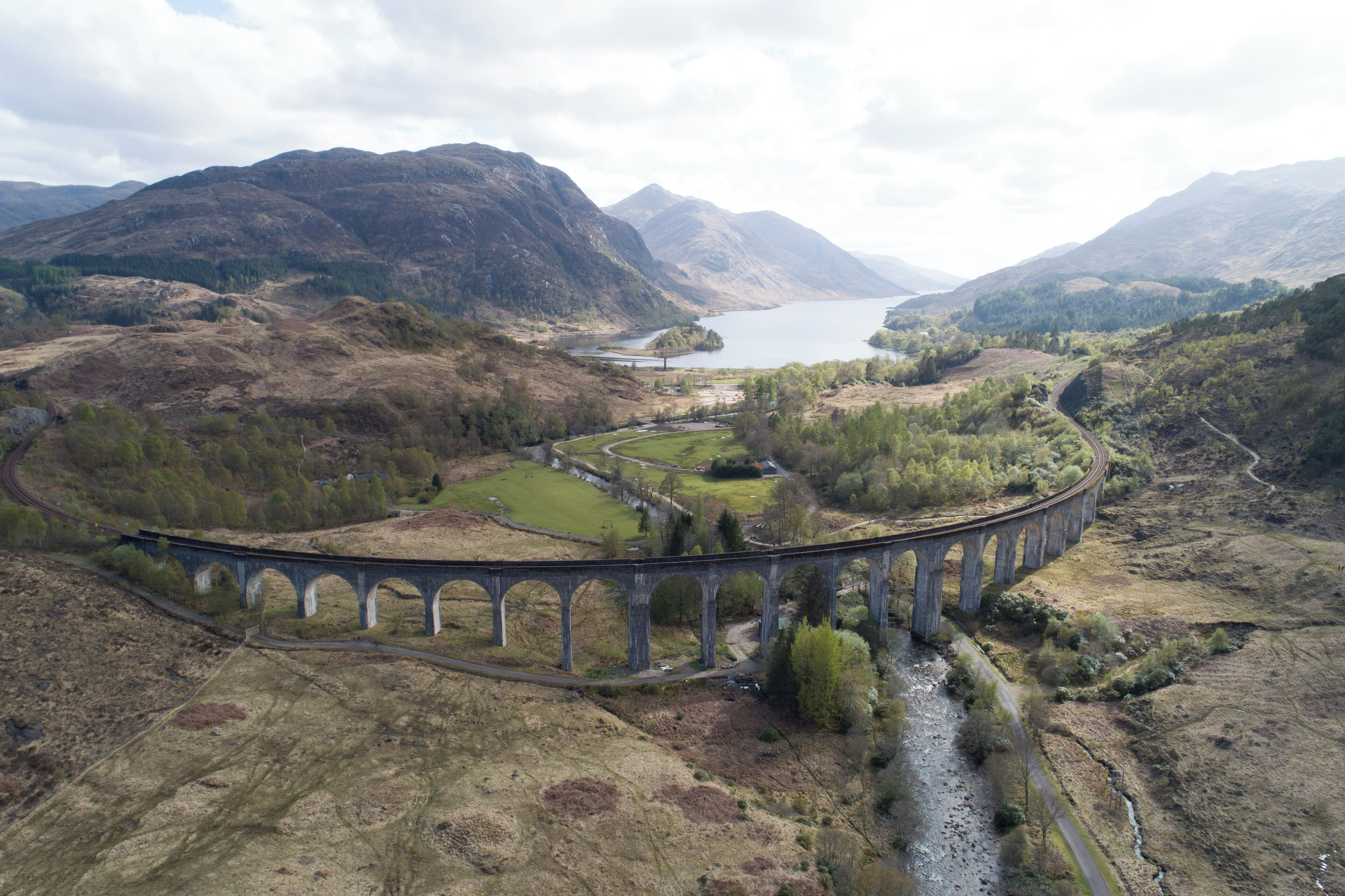 A stone viaduct over a river, surrounded by hills and a lake.