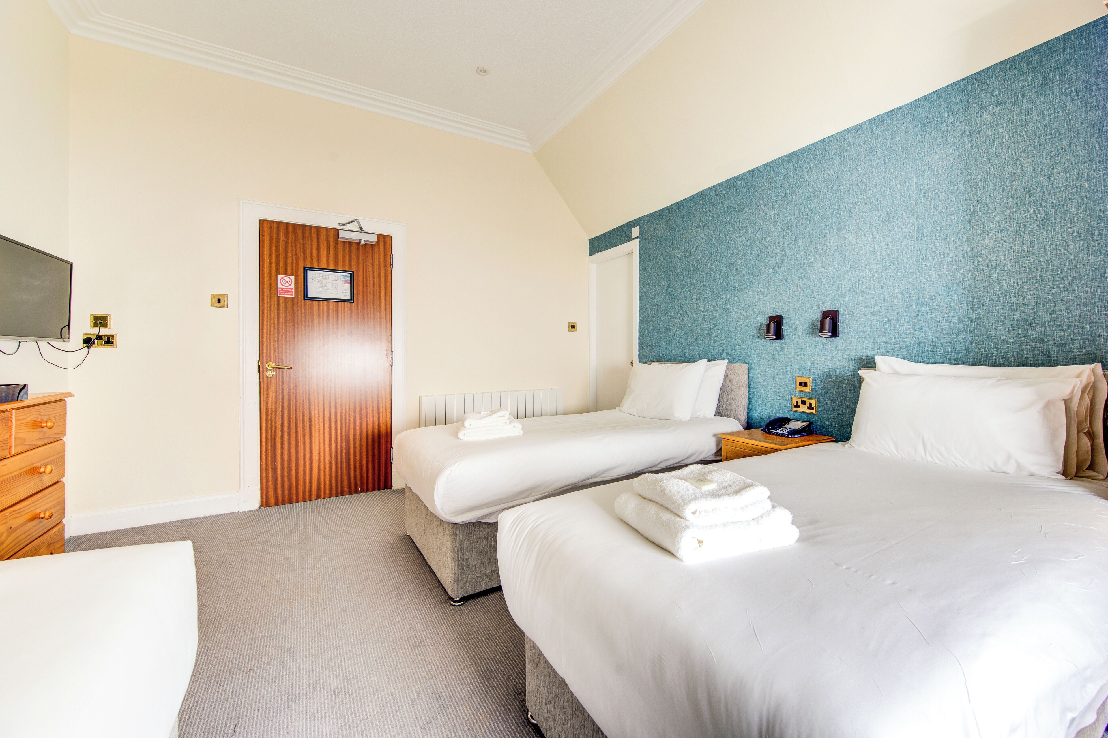 A hotel room with two beds, a wooden dresser, a television, and a blue accent wall.