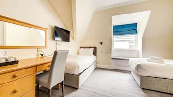 A hotel room with a wooden desk, a chair, two beds, a television, and a window with a blue curtain.