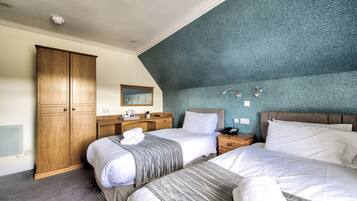 A hotel room with two beds, a wooden wardrobe, a vanity with a mirror, and a blue textured wall.