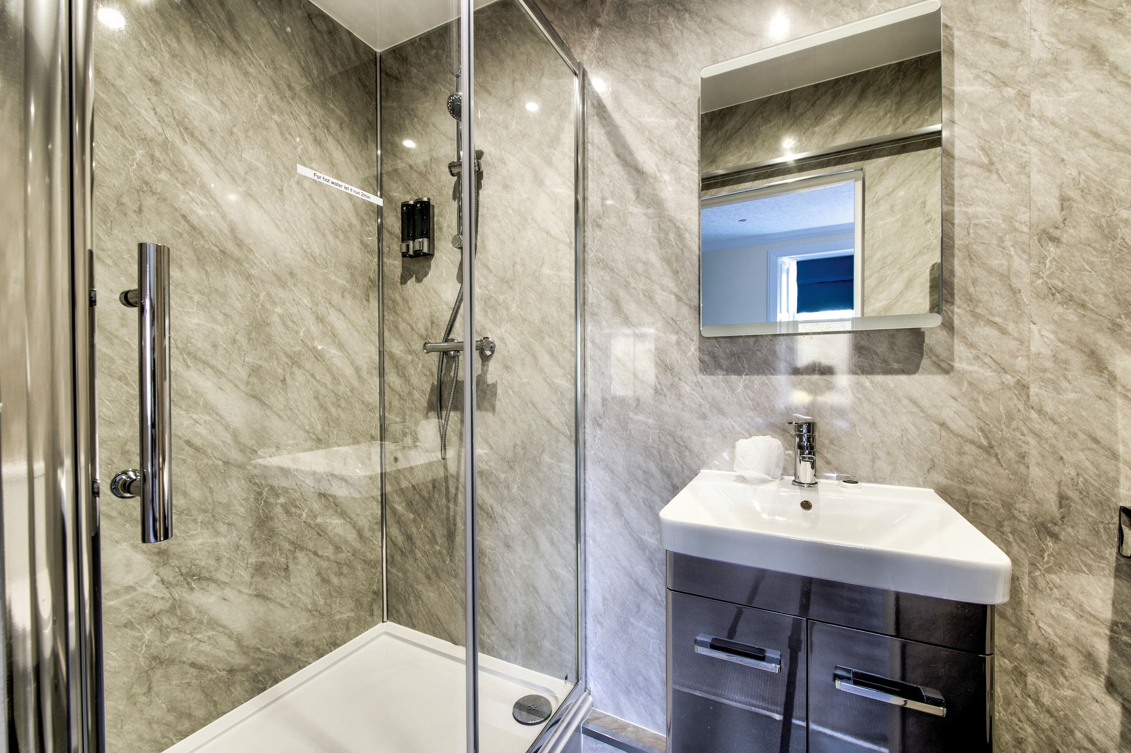 A modern bathroom with a glass-enclosed shower, a white sink, and a marble wall.