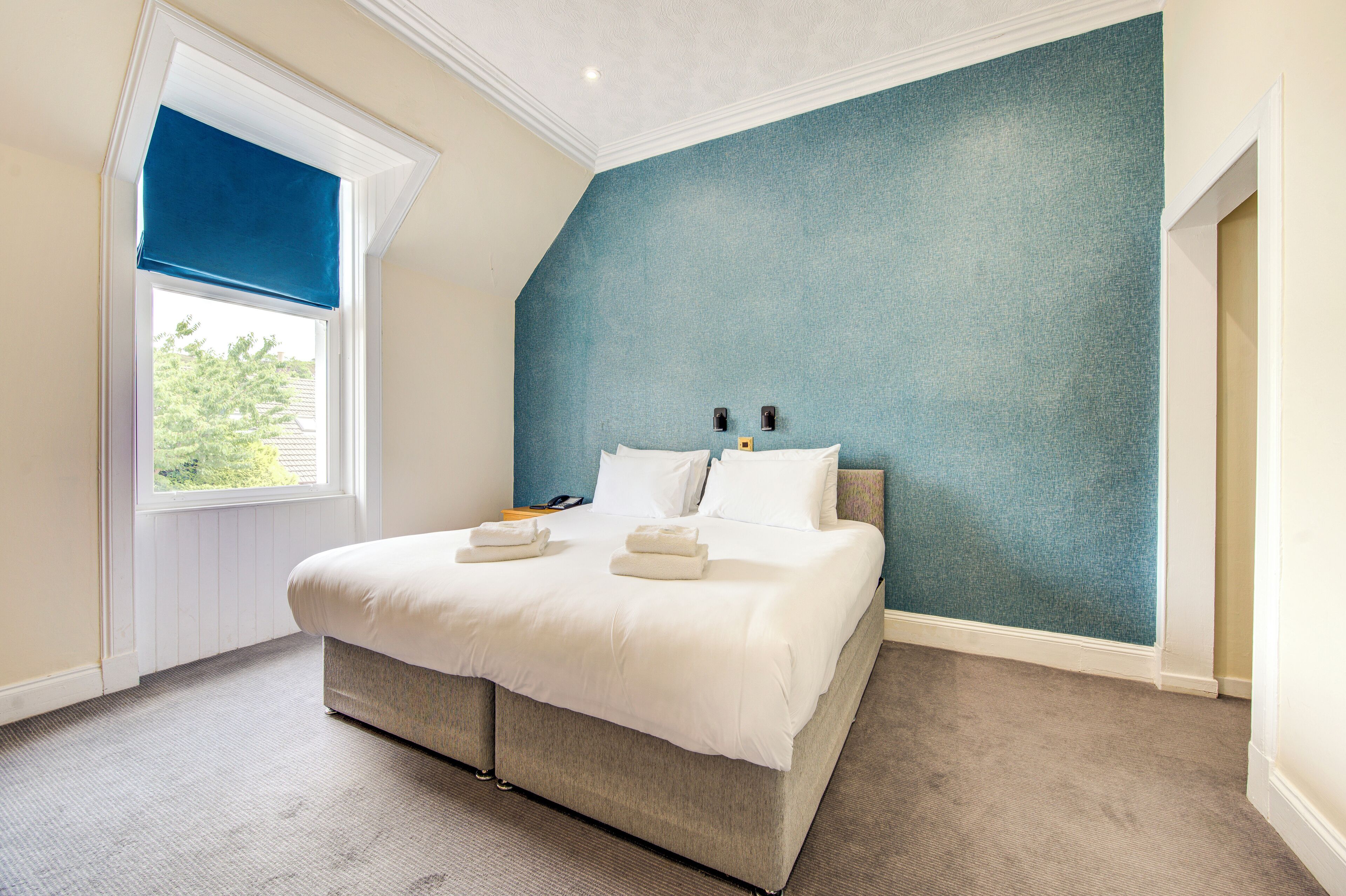 Un dormitorio con cama, ventana con persiana azul y pared texturizada en tono azul.