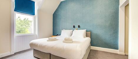 Un dormitorio con cama, ventana con persiana azul y pared texturizada en tono azul.