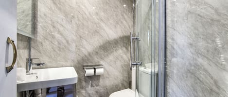 A modern bathroom with a marble wall, a white sink, a glass shower enclosure, and a toilet.