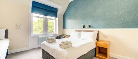 A bedroom with a large bed, a bedside table, a window with blue curtains, and a wall with a textured pattern.
