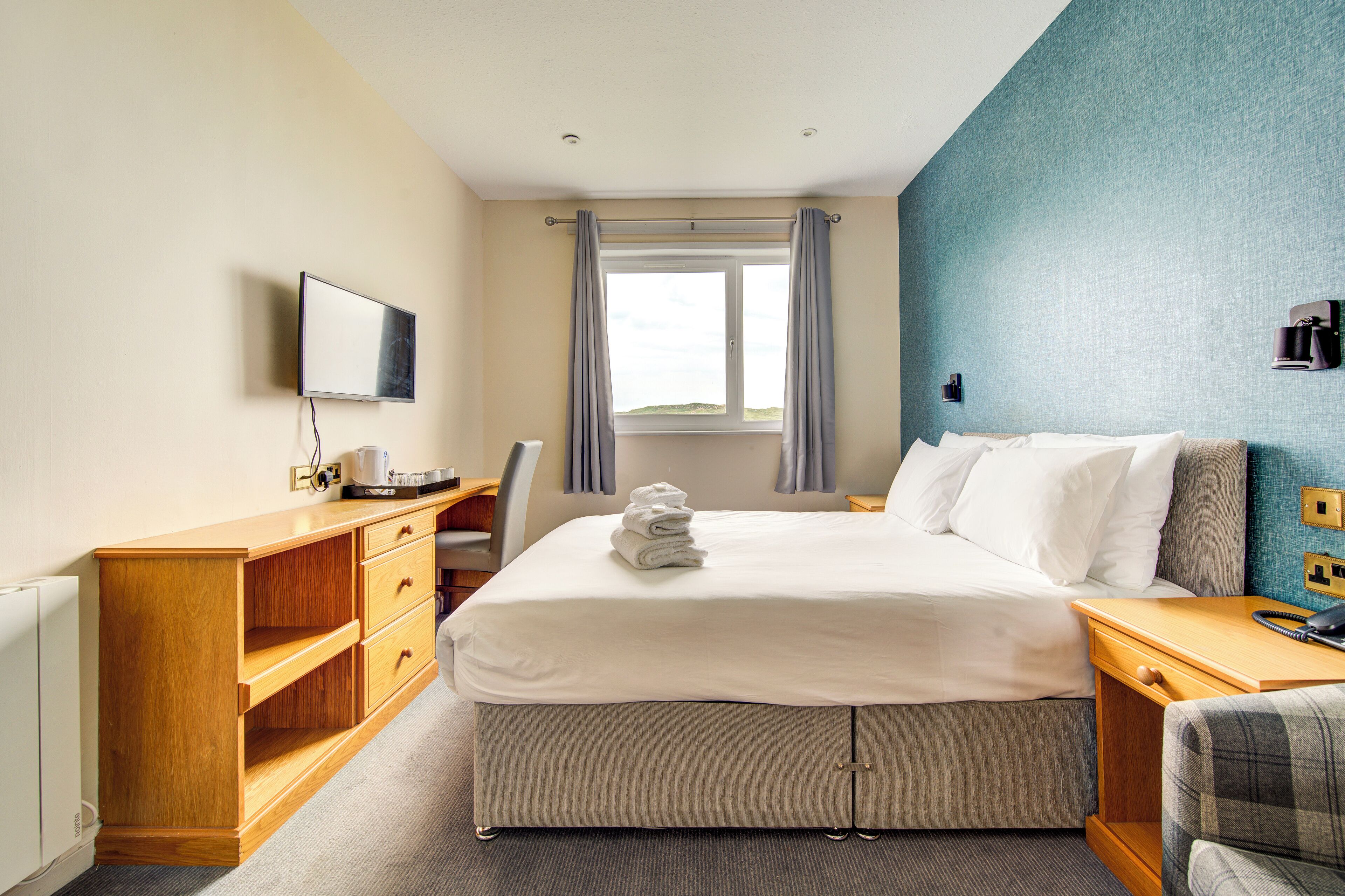 A hotel room with a bed, a desk, a chair, a television, and a window with curtains.
