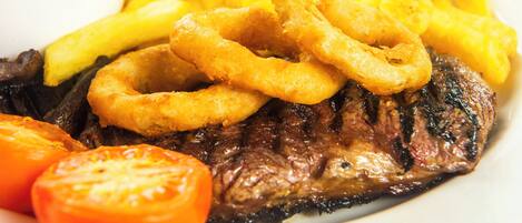 A steak with onion rings and fries on a plate.
