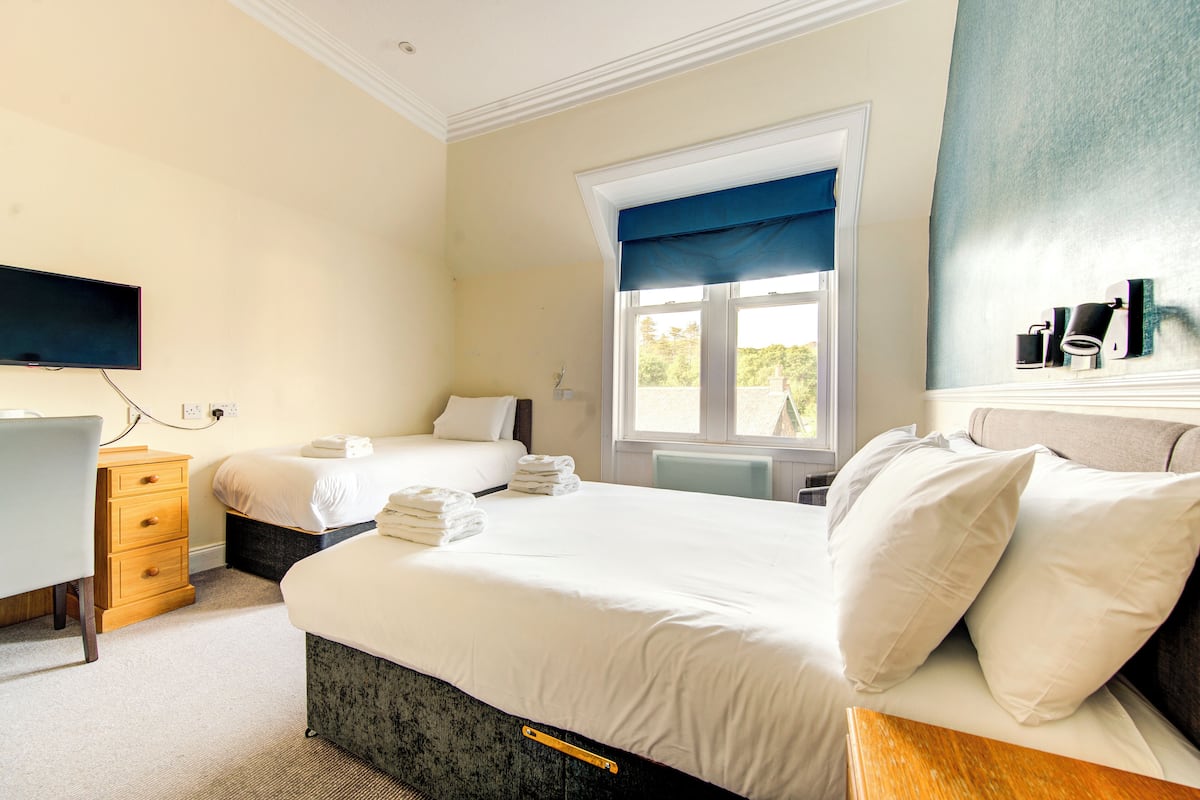 Quarto de hotel com uma cama grande, uma escrivaninha e uma janela com vista.
