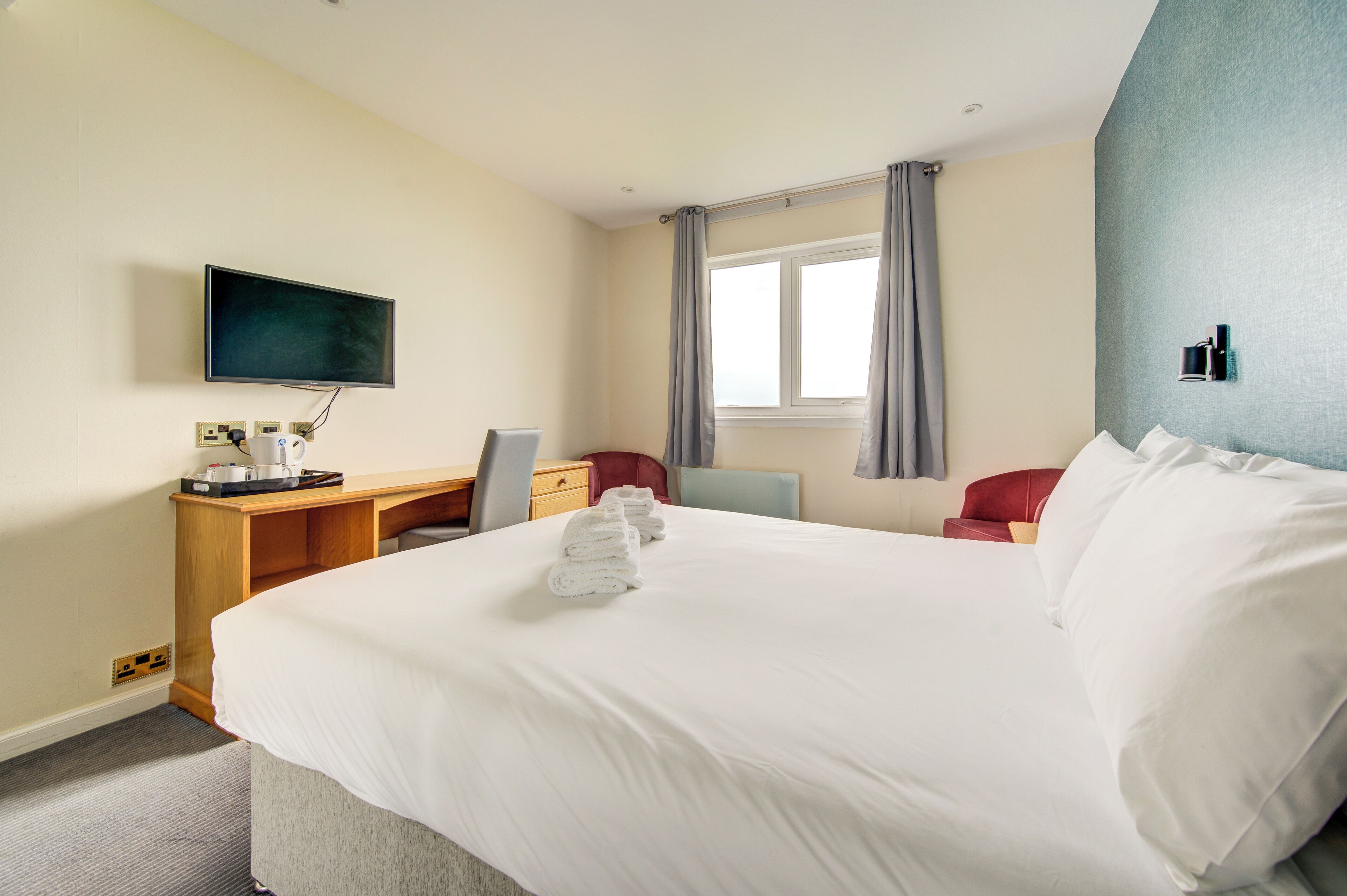A hotel room with a bed, a desk, a chair, a television, and a window with curtains.