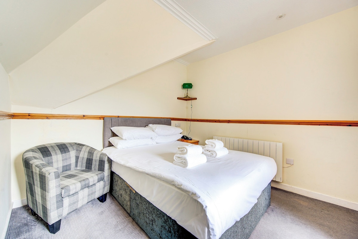 A bedroom with a bed, a chair, a radiator, and a green lamp on a shelf.
