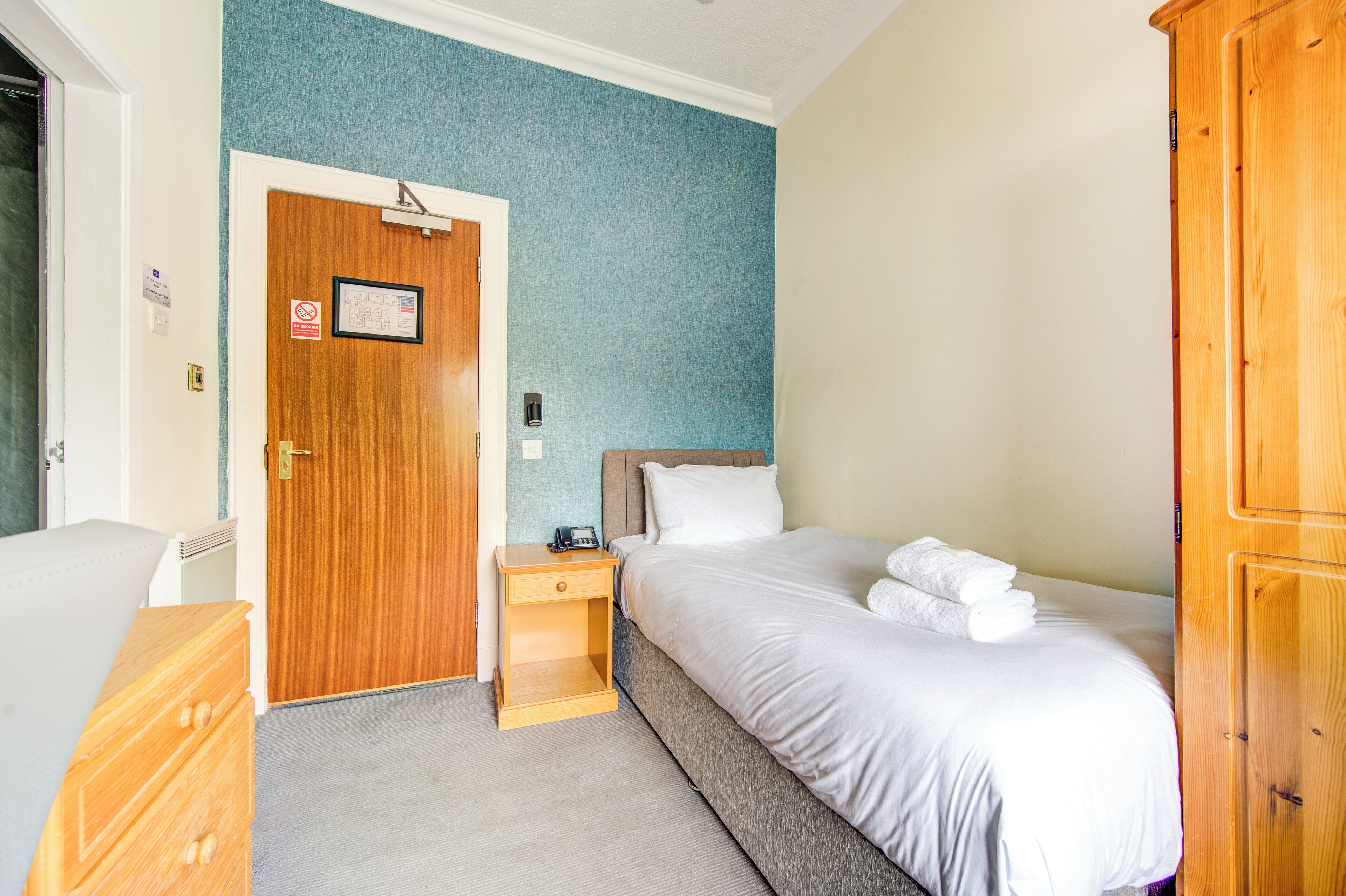 Una habitación de hotel con cama, mesita de noche de madera, armario y una puerta con un cartel.