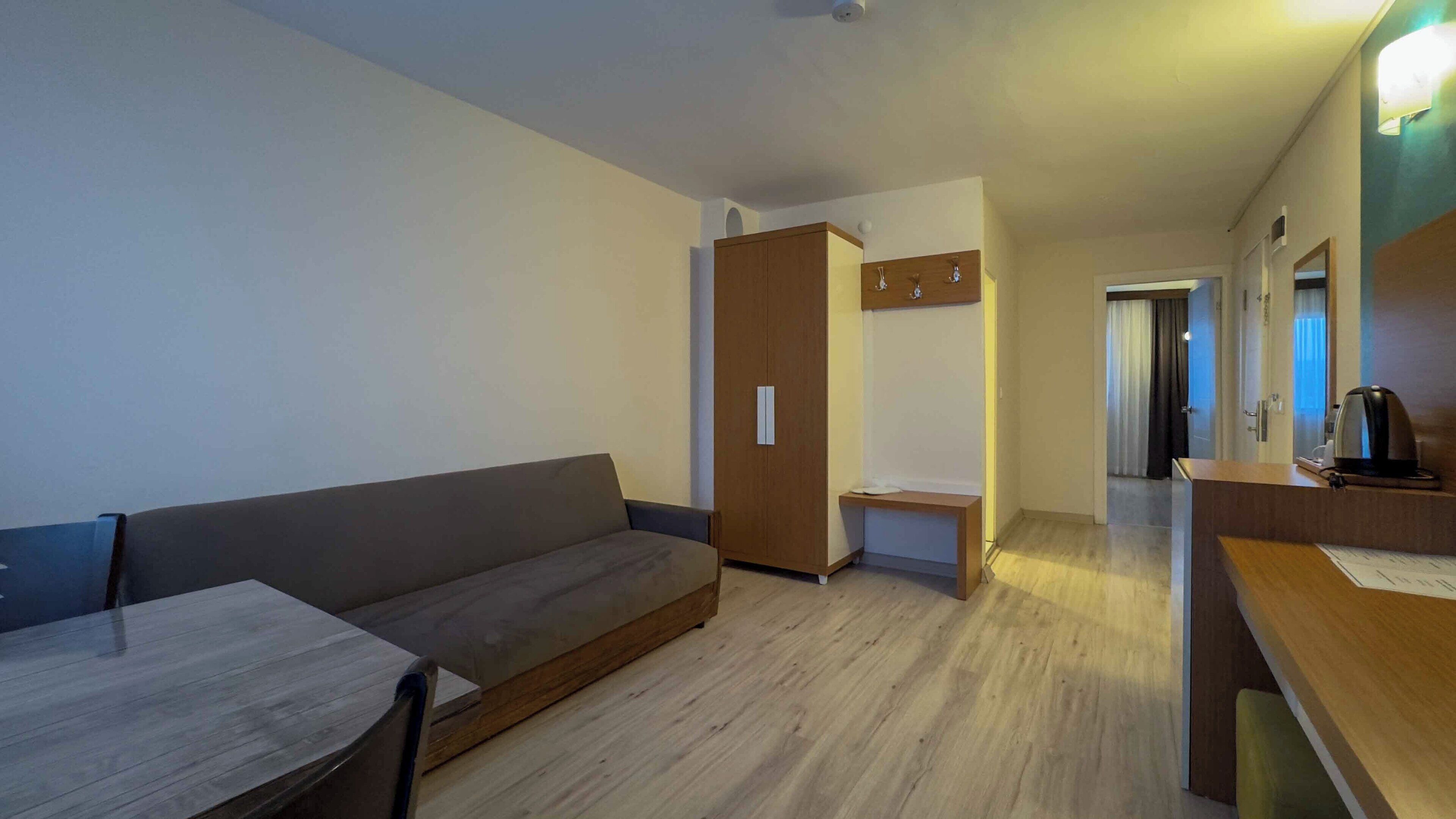 Een moderne hotelkamer met een bank, een klein tafeltje, een houten kledingkast en een kitchenette.