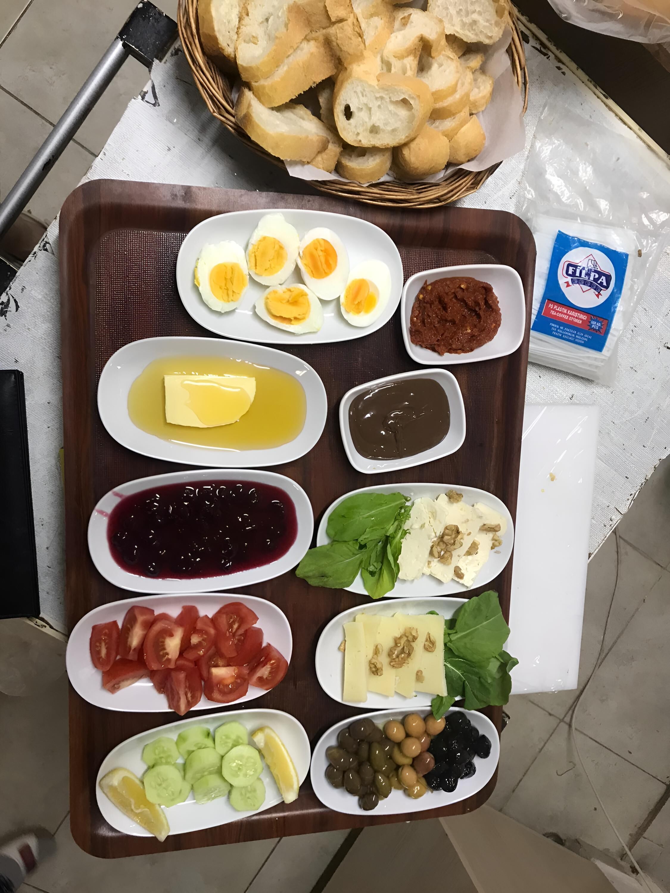 Uma bandeja com diversos alimentos, incluindo ovos, manteiga, chutney, tomates, pepinos, azeitonas, queijo e pão.