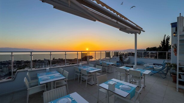 A rooftop terrace with tables and chairs, overlooking a sunset view. - La Bella Suite Hotel (Kusadasi)